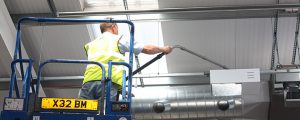 man using a cherry picker to clean above an air conditioning vent as part of a deep cleaning service