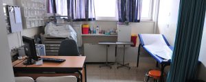 a doctor's treatment room, with a blue bed, desk and medical supplies