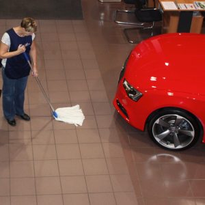 woman providing showroom cleaning services by cleaning a floor with mop in a car showroom