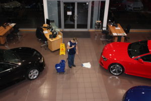 a woman providing showroom cleaning services by mopping a floor in a car showroom