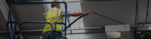 a man providing professional deep cleaning services on a cherry picker using a vaccuum cleaner to clean the top of an air conditioning unit