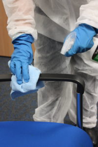 a cleaner in PPE wiping a chair handle with antiviral spray