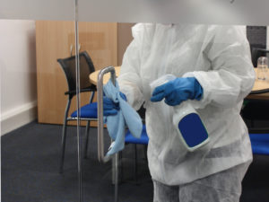 woman in PPE cleans the handle of a glass door as part of a covid deep clean
