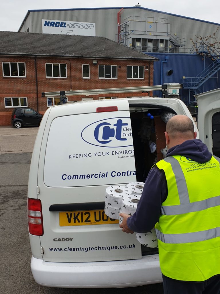 man in yellow visibility vest hands toilet roll supplies into the back of Cleaning Technique's van.