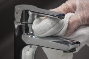 detail of hand cleaning a tap with a white cloth
