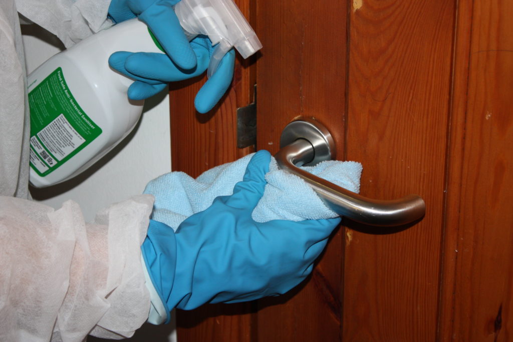 close up of gloved hand disinfecting door handle