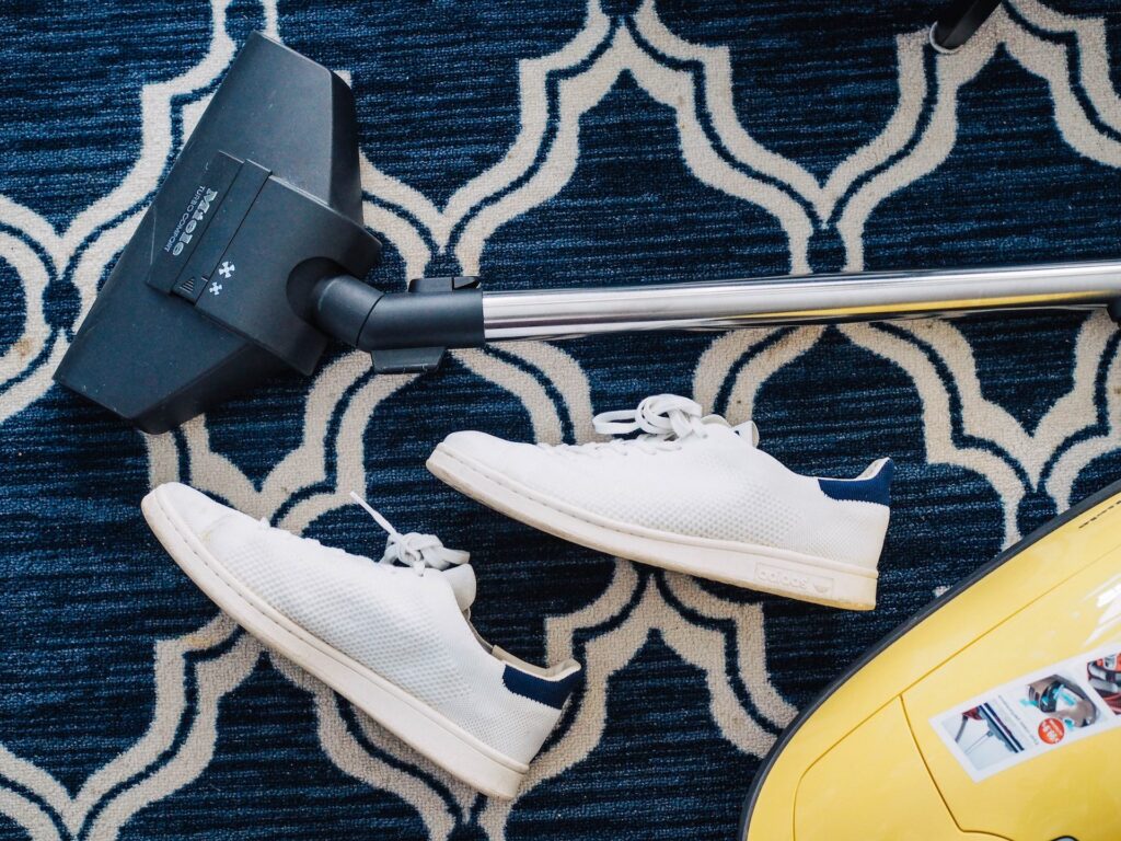 vacuum cleaner laying on blue carpet with trainers.
