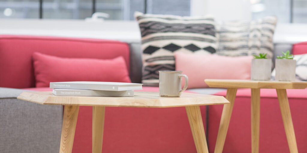Red couch with cushions and two wooden tables in front of it. The tables have books and mugs on them.