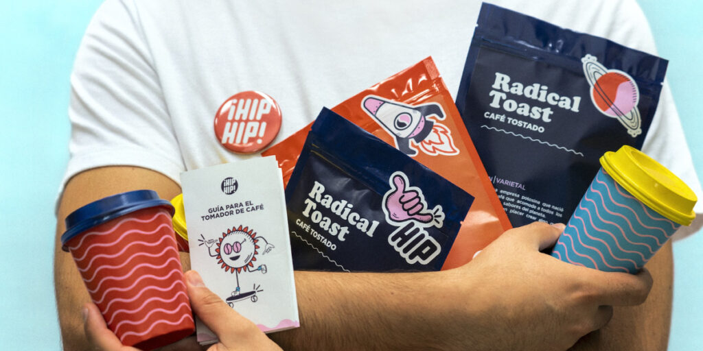 Image showing a close up of a man in a white t-shirt, with his arms folded, holding branded products and cups, with a pale blue background.