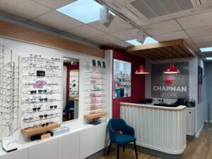 Image showing the optician shop floor, with glasses on display shelves, a tall mirror, a blue chair and a cash desk