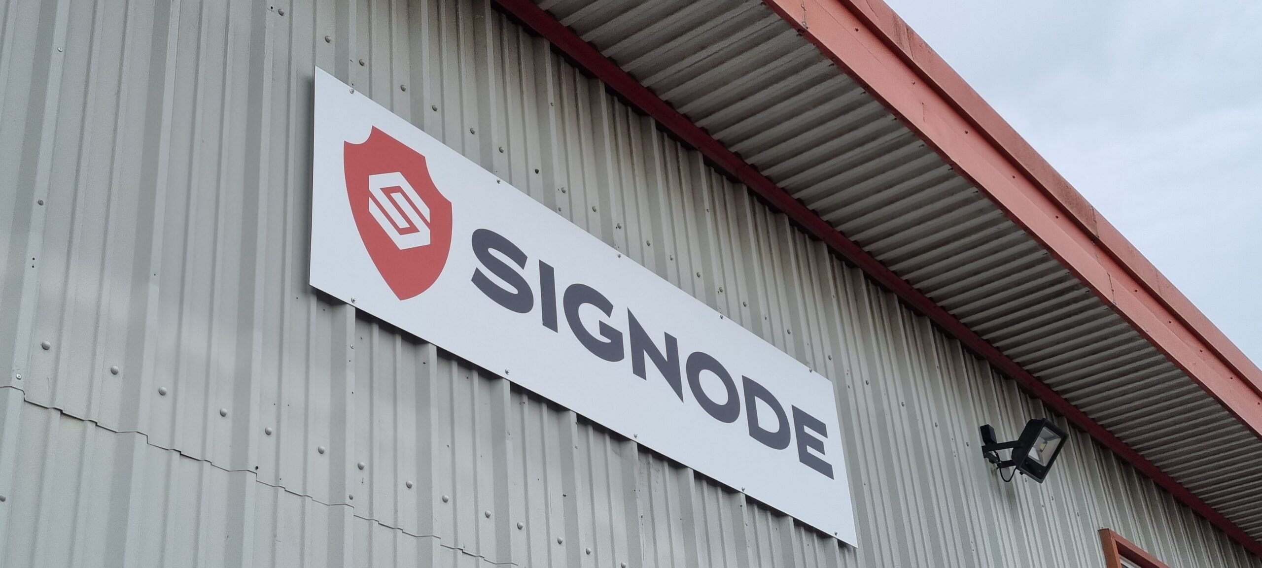 Photograph looking up at a grey corrugated industrial building with a sign that reads “Signode”