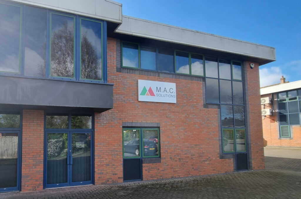 Photograph of MAC Solutions offices in Redditch, showing a brick building with blue window frames an a sign above the door with the MAC logo