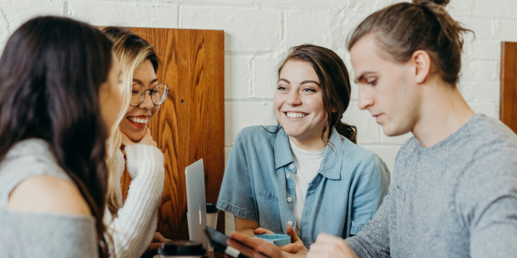 Four employees smiling, drinking coffee together - following tips on how to improve staff wellbeing could look like this
