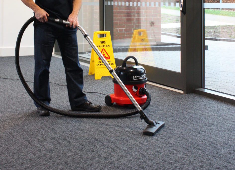 A cleaning operative vaccuums a carpet in a church reception area