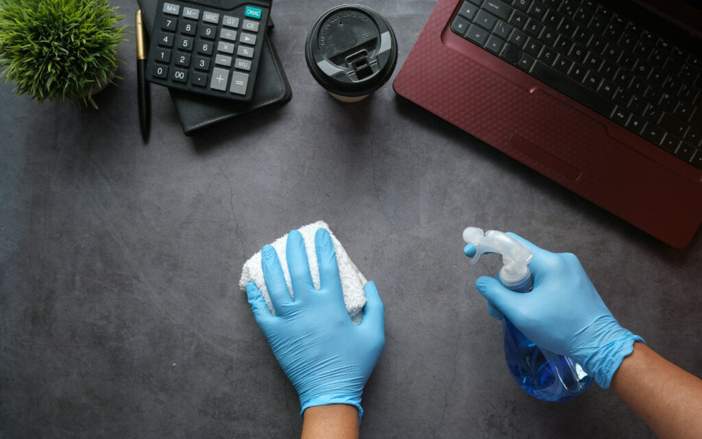 bird's eye view of two hands in blue gloves conducting office cleaning on an office desk.