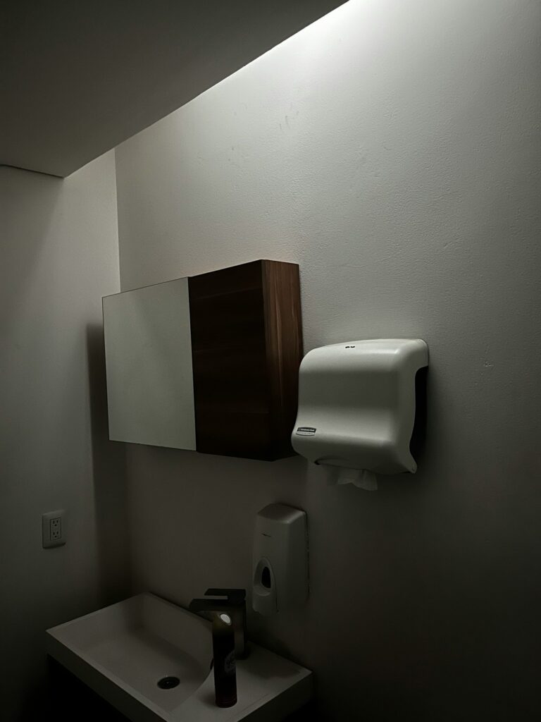 A sink, hand dryer and cabinet on a wall.